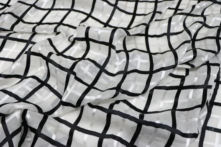 a close-up view of a fabric with a black and white checkered pattern. The fabric appears to be made of a sheer material, with a grid-like design that creates a visually striking pattern.