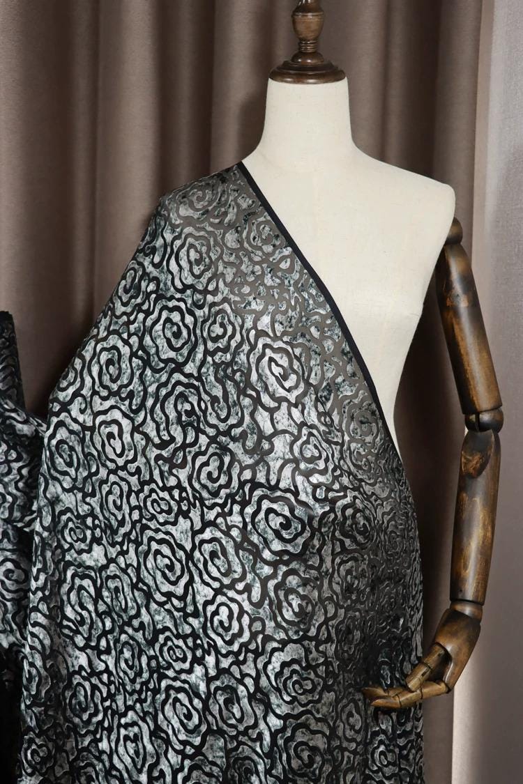 A mannequin wearing a black and silver patterned fabric draped over its body.