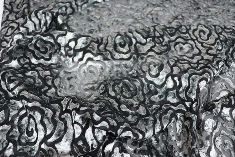 a close-up view of a fabric with a repeating pattern of black and white swirls or curves. The pattern appears to be a floral or abstract design, with the black and white colors creating a visually striking contrast.