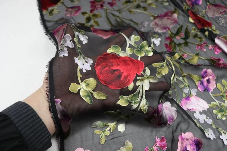 A hand is holding a piece of fabric with a floral pattern, featuring red and pink flowers against a black background.