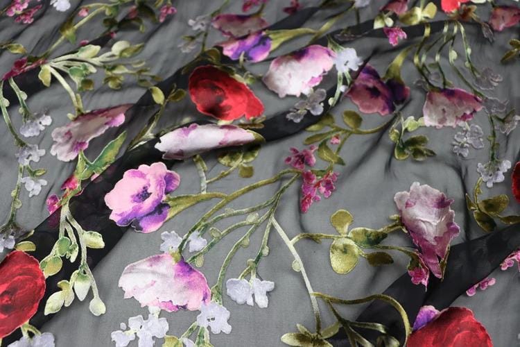 a close-up view of a fabric with a floral pattern, including red, pink, and white flowers. The fabric appears to be black, with the flowers and leaves creating a visually striking contrast against the dark background.