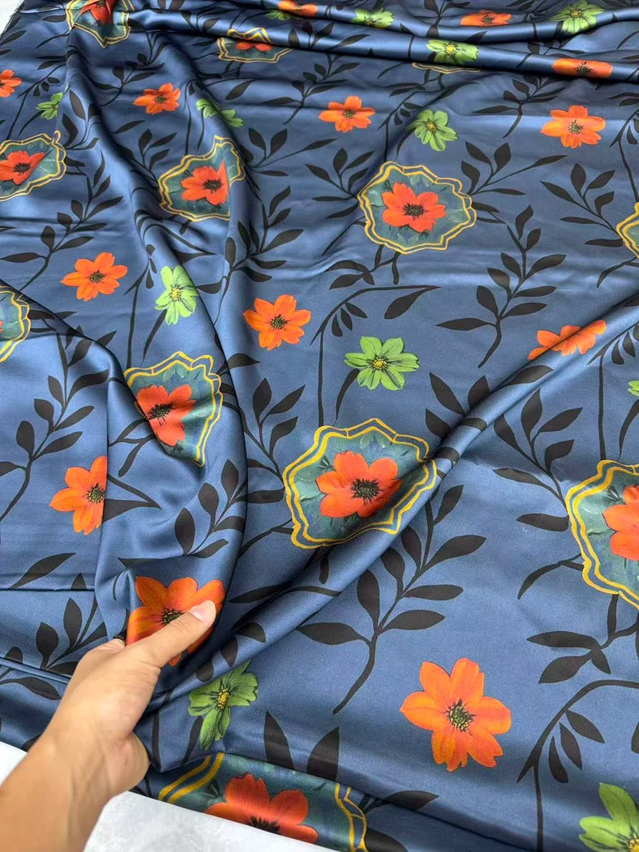 a hand holding a piece of fabric with a floral pattern on it. The fabric has a blue background with orange and green flowers and leaves.