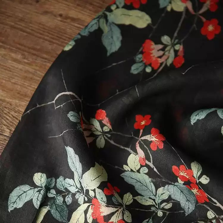 a close-up view of a black fabric with a floral pattern of red flowers and green leaves.