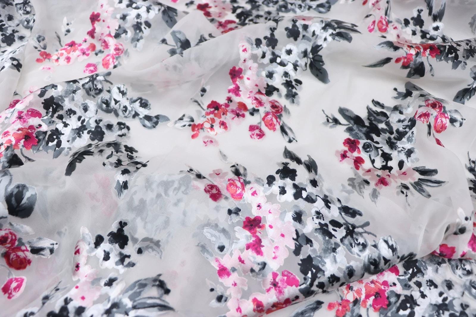 a close-up view of a fabric with a floral pattern in shades of pink, black, and white. The pattern appears to be a mix of different flowers and leaves, creating a visually appealing and intricate design.