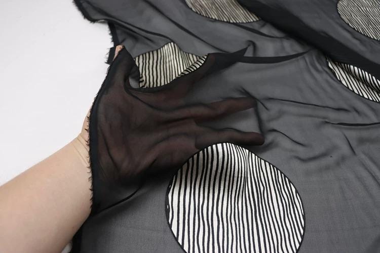 A hand is holding a black and white striped fabric with circular patterns.