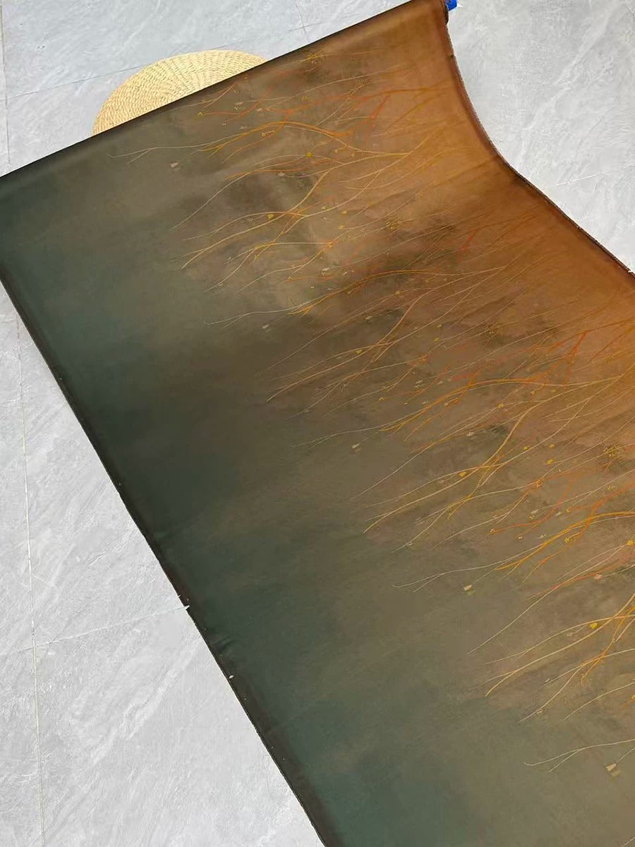 a piece of fabric with a gradient of colors, including shades of green, brown, and orange. The fabric appears to be a piece of cloth or textile, with a pattern or design on it. The fabric is placed on a surface, possibly a table or countertop, and there is a straw hat visible in the background.