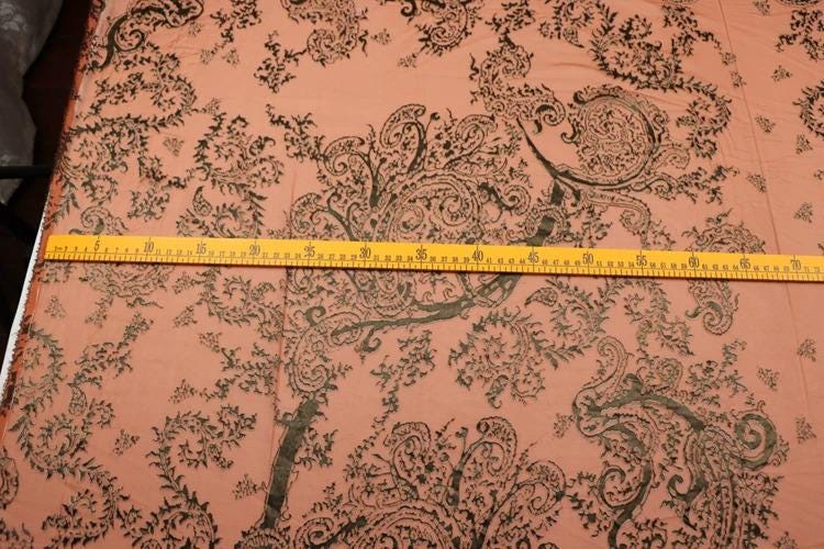 a close-up view of a fabric with a paisley pattern, and a yellow measuring tape is placed across the fabric to measure its length.