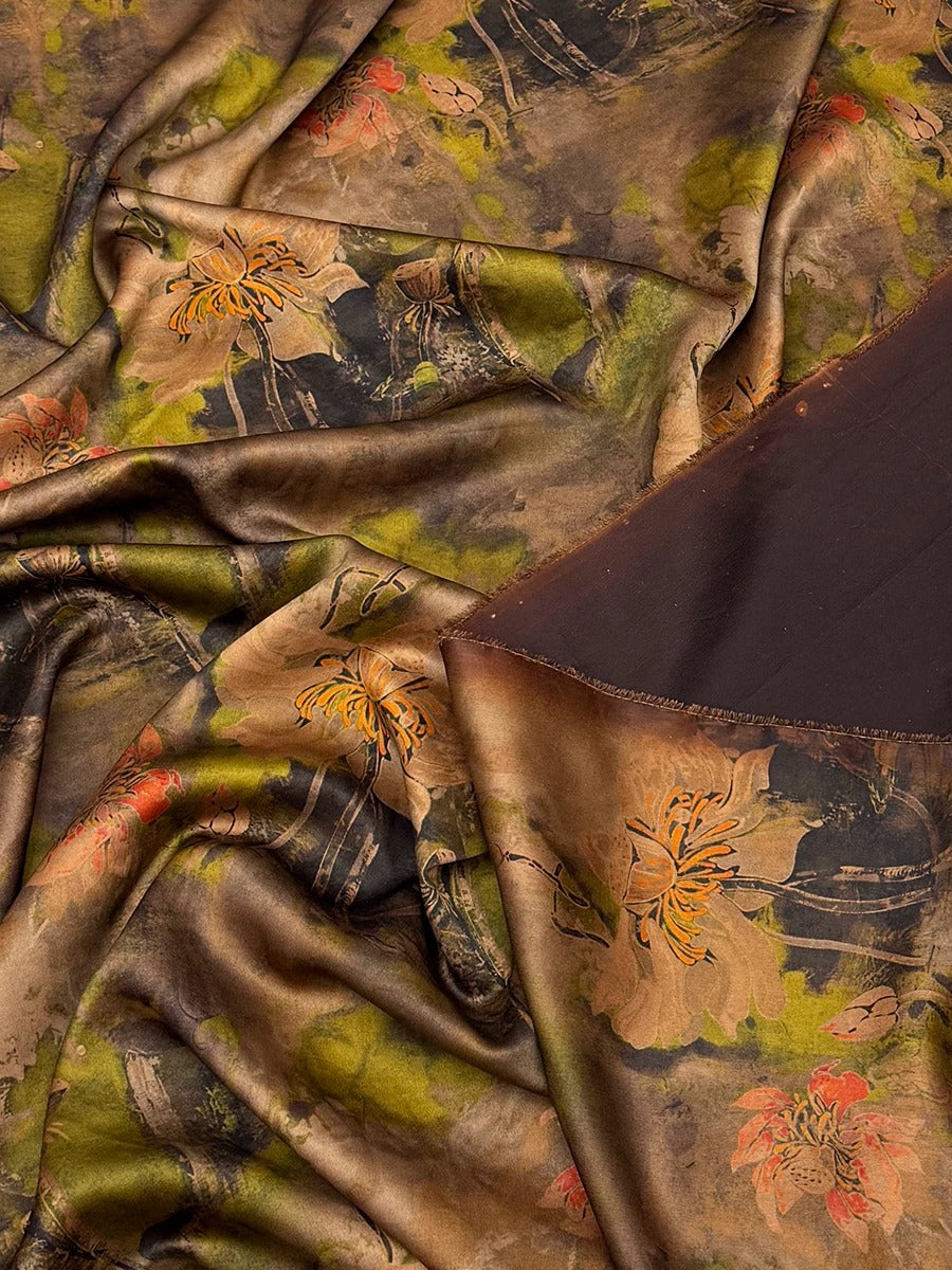 a close-up view of a fabric with a floral pattern, featuring a mix of green, brown, and orange colors. The fabric appears to be made of silk or a similar material, and it is crumpled, giving it a textured and soft appearance.