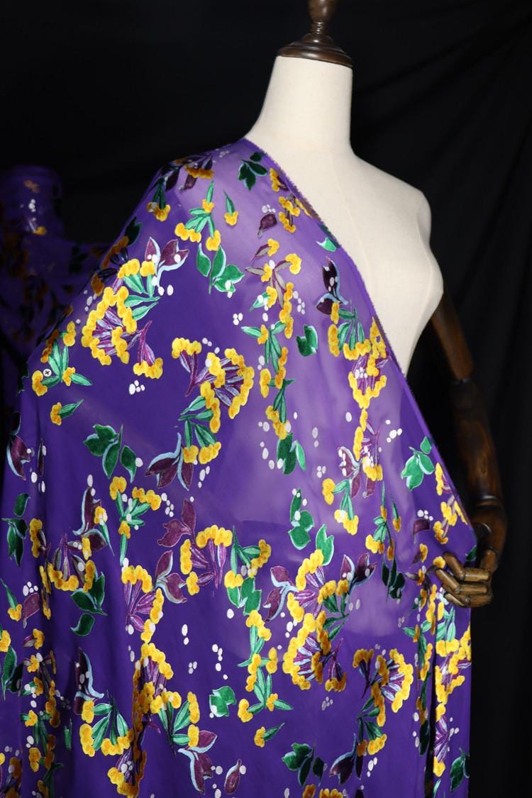 A mannequin wearing a purple fabric with a floral pattern in shades of purple, yellow, and green.