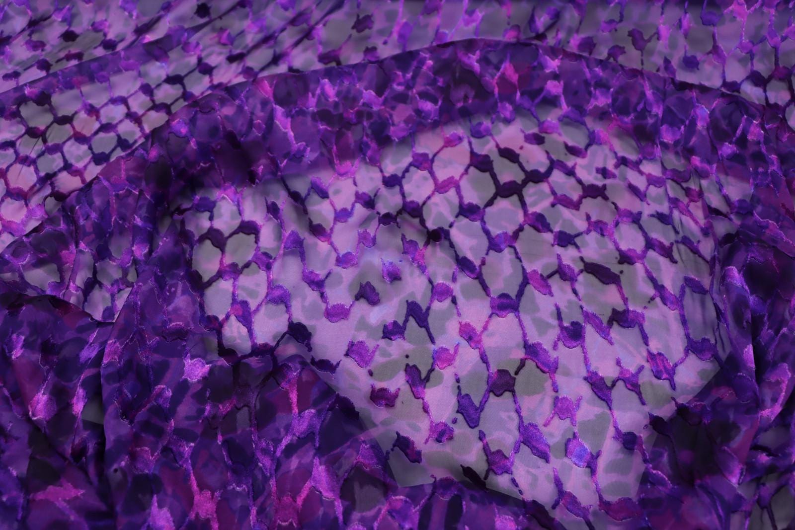 a close-up view of a fabric with a purple and white pattern, featuring a repeating geometric design.
