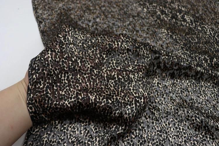 A close-up view of a hand holding a piece of fabric with a leopard print pattern.
