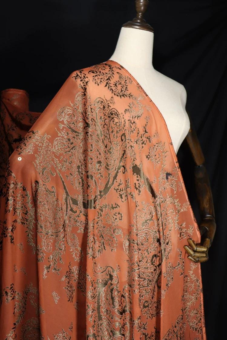 A mannequin wearing a vibrant orange and black patterned fabric draped over its body.