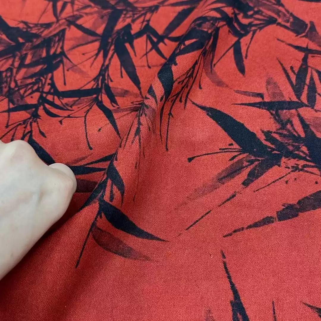 a close-up view of a fabric with a striking red background and a black leaf pattern. The fabric appears to be made of silk, and the leaf pattern is visible in various shades of black. The image does not contain any text or additional objects, and the focus is solely on the fabric and its design.