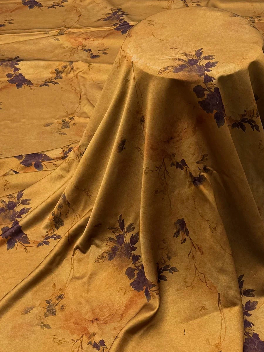 a close-up view of a fabric with a floral pattern, featuring a mix of purple and orange colors. The fabric appears to be folded or draped, creating a sense of depth and texture.