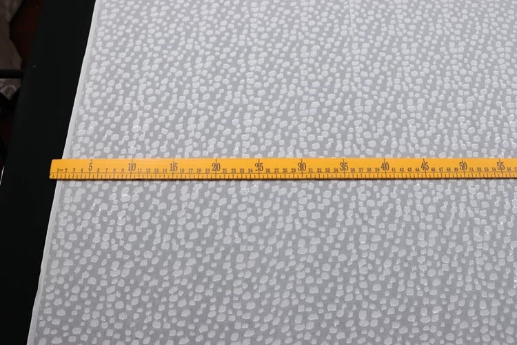 a yellow measuring tape stretched across a white surface with a pattern of small dots or circles.