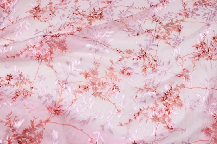a close-up view of a fabric with a pink floral pattern. The fabric appears to be made of sheer material, with delicate pink flowers and leaves covering the entire surface. The pattern is intricate and detailed, showcasing the craftsmanship of the fabric.