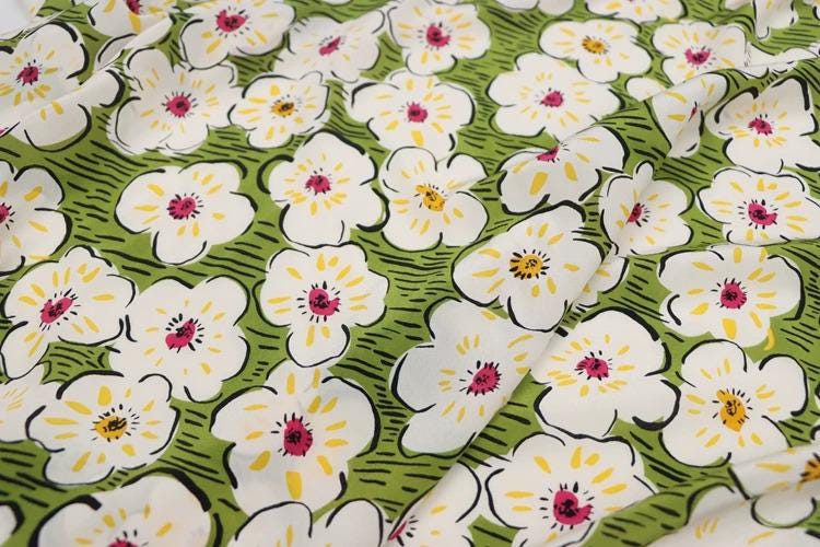 a close-up view of a fabric with a repeating pattern of white flowers with yellow centers against a green background.