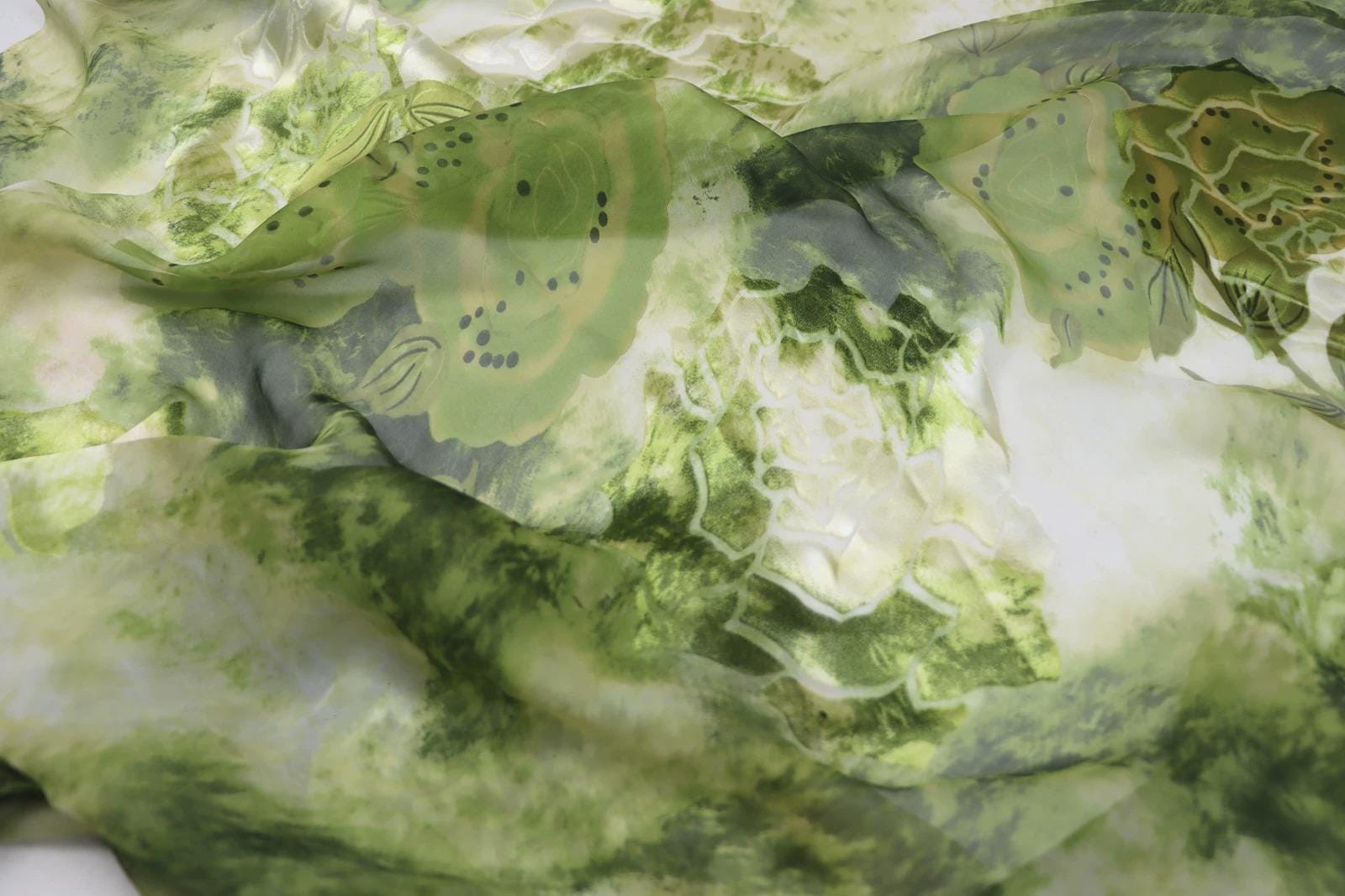 The image is a close-up of a fabric with a green and white floral pattern. The fabric appears to be made of silk or a similar material, and it has a slightly wrinkled texture. The pattern consists of various shades of green and white, creating a visually interesting and vibrant design.