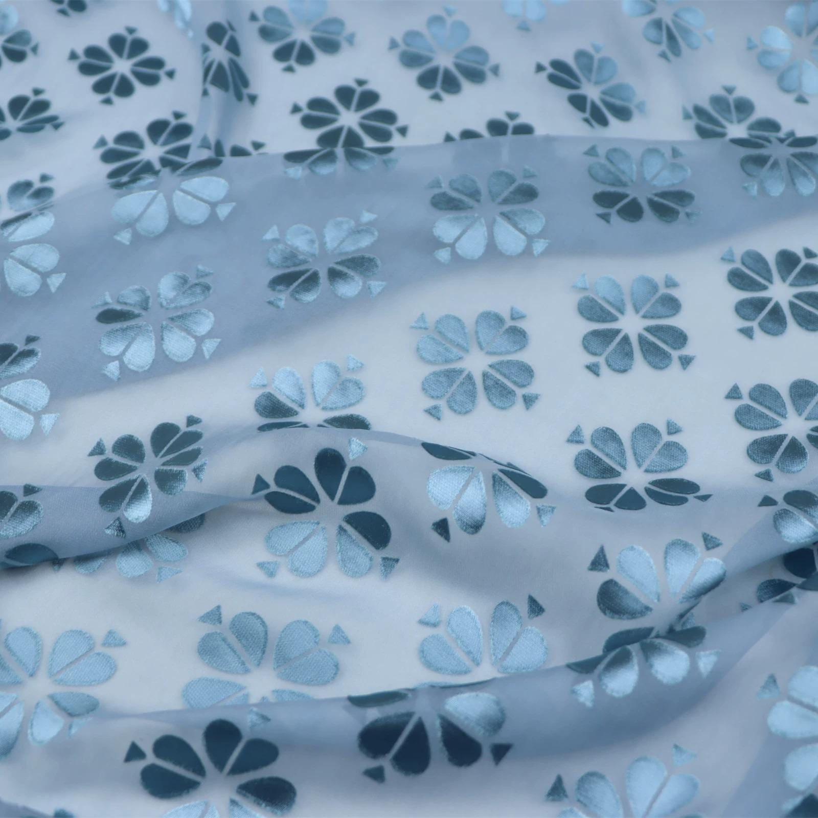 a close-up view of a fabric with a repeating pattern of blue and white flower-like shapes.