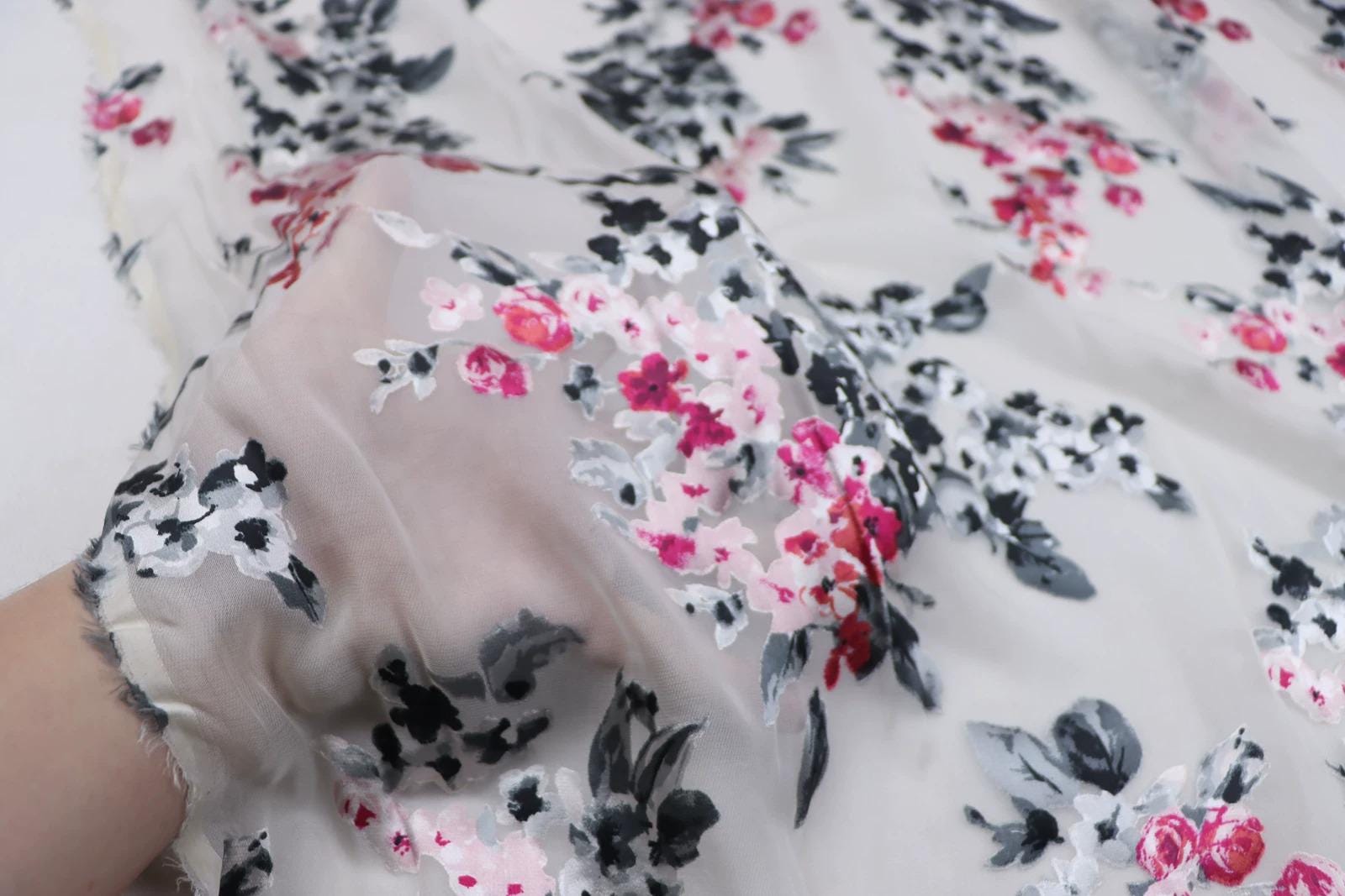 a close-up view of a fabric with a floral pattern in shades of pink, black, and white. The fabric appears to be a sheer material, with the flowers and leaves appearing in a delicate and intricate design.
