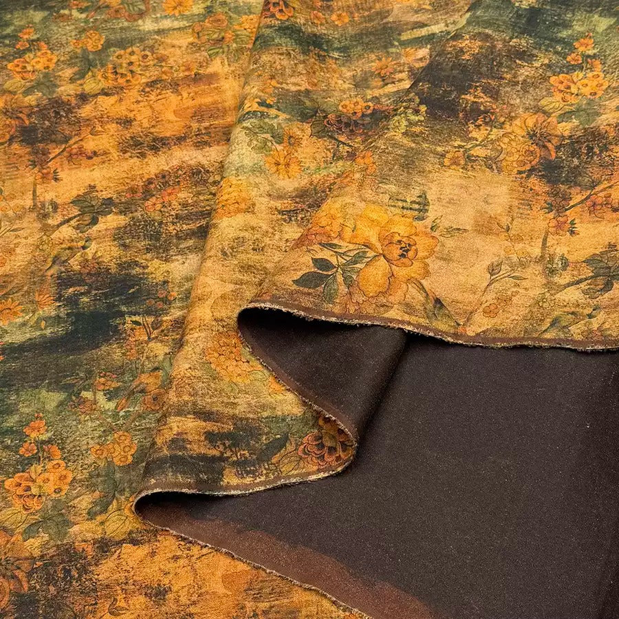 a close-up view of a fabric with a floral print in shades of green and brown. The fabric appears to be a piece of cloth or textile, with a dark brown or black background.