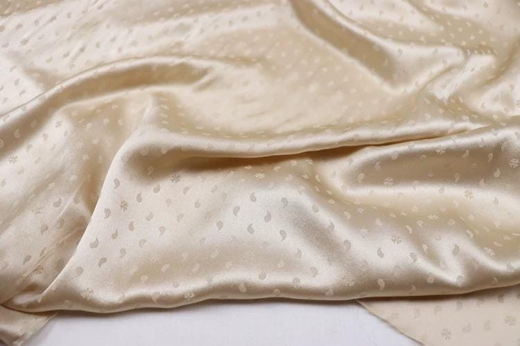 a close-up view of a crumpled, light-colored fabric with a repeating pattern of small white dots or circles.