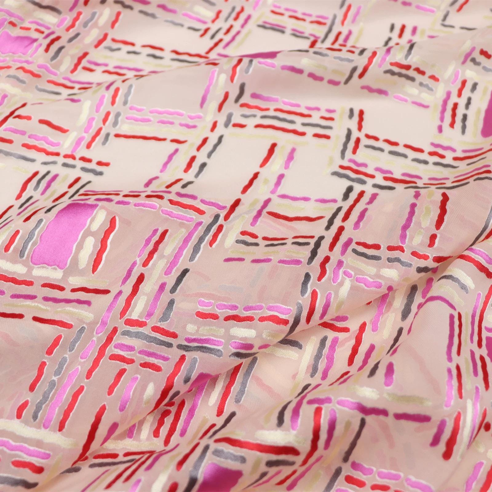a close-up view of a fabric with a colorful, abstract pattern of intersecting lines and shapes in various shades of pink, red, and gray.