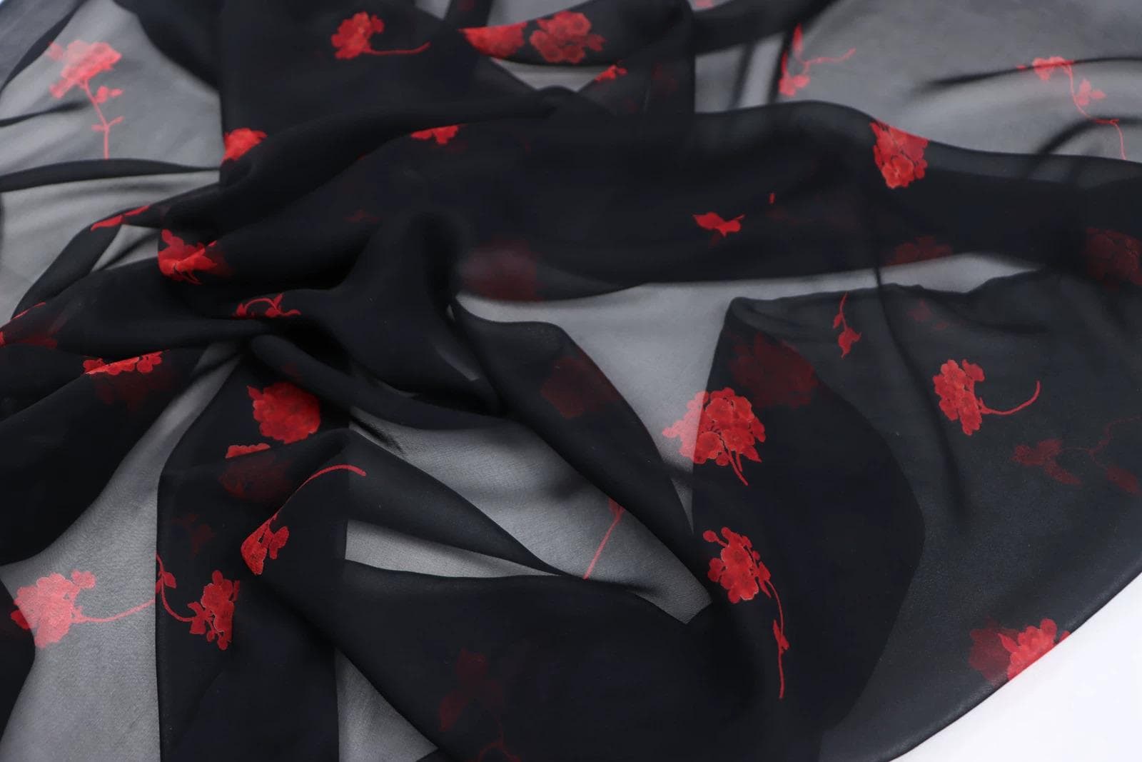 a close-up view of a black fabric with red floral patterns. The fabric appears to be made of silk or chiffon, and the red flowers are scattered across the fabric in a random pattern.