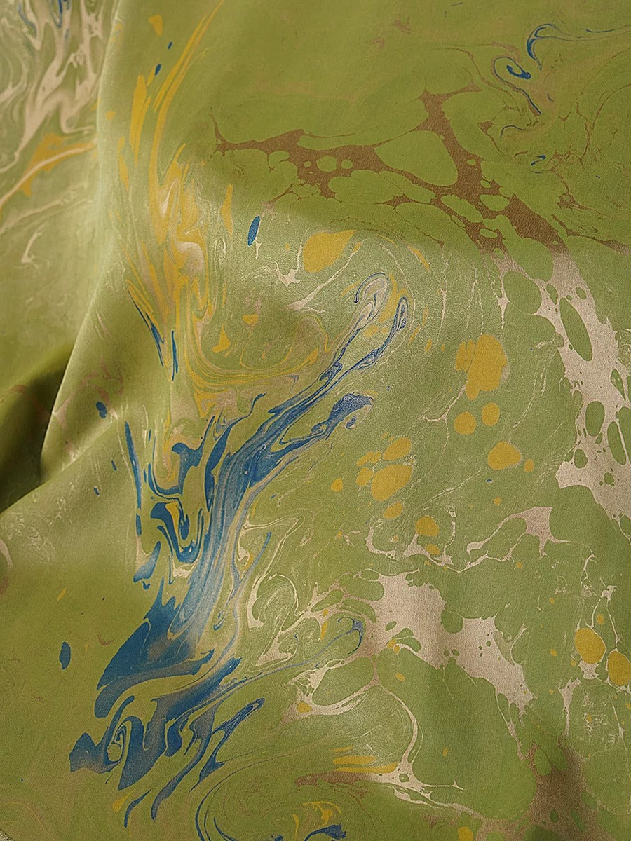 The image is a close-up of a fabric with a marbled pattern in shades of green, blue, and yellow. The fabric appears to be made of a material with a marbled effect, giving it a textured and visually interesting appearance.