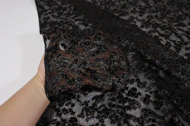 A hand is holding a piece of black fabric with a floral pattern.
