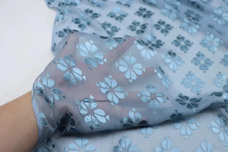 A hand is holding a piece of fabric with a repeating pattern of blue flowers on it.