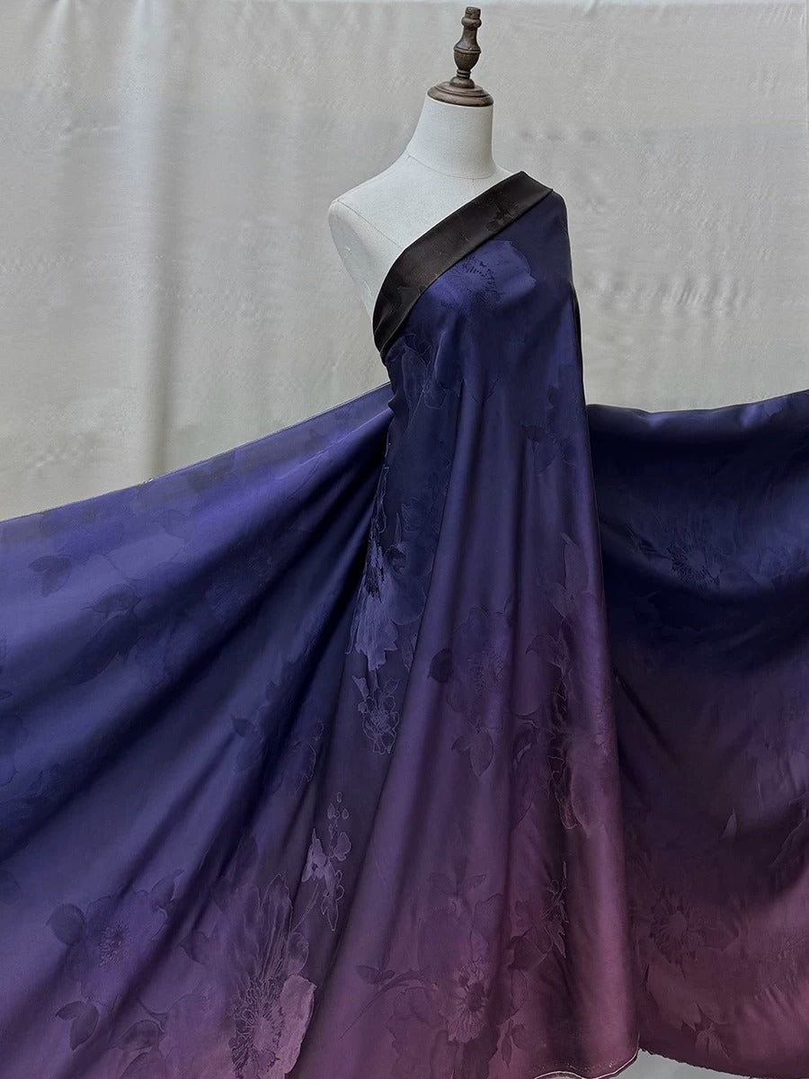 A mannequin wearing a long, flowing purple dress with a floral pattern. The dress has a black belt and appears to be made of a shiny, satin-like fabric.